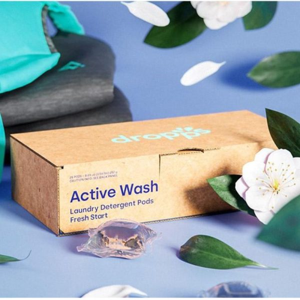 box of Dropps Laundry pods with a couple loose pods on a blue table cloth with clothes and flowers
